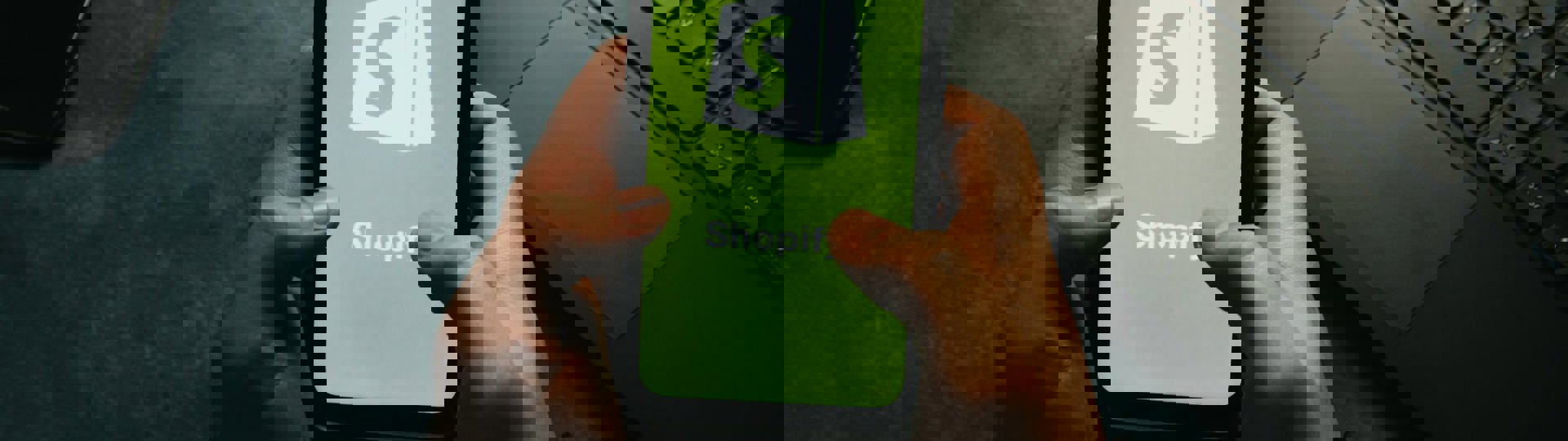 Hands Holds A Cell Phone Showing The Shopify Logo